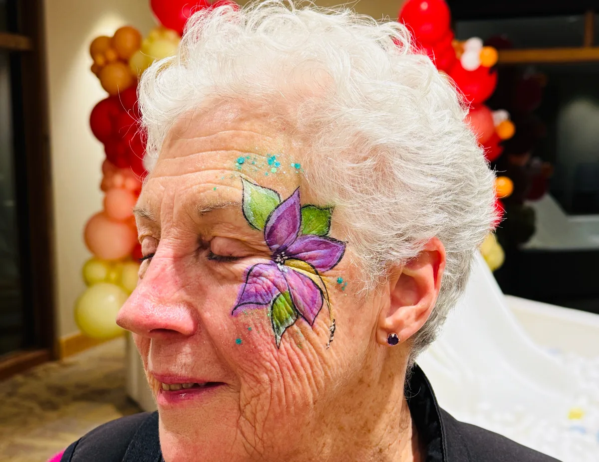 Older woman with purple butterfly face painting close-up.