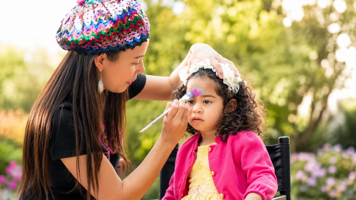 Colory Faces artist painting a young child at an outdoor event.